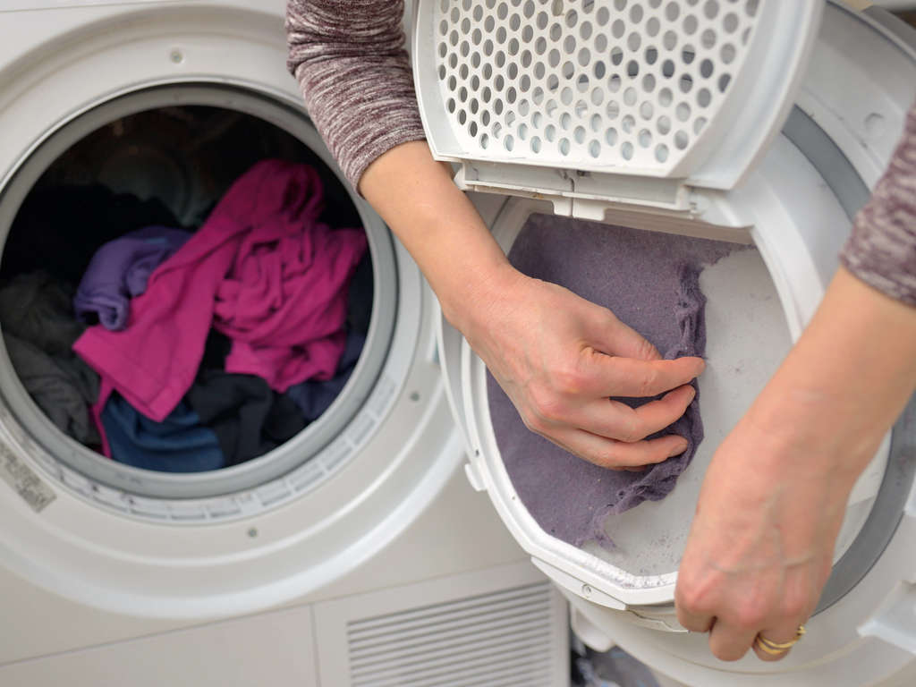 A person is putting clothes in the dryer.