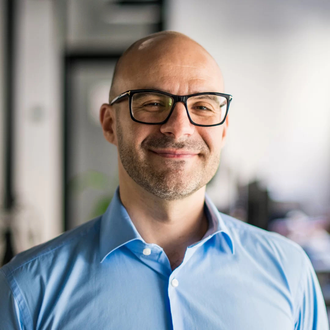 A man with glasses and bald head wearing a blue shirt.