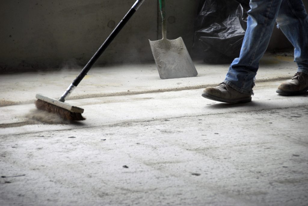 A person sweeping the floor with a broom and shovel.