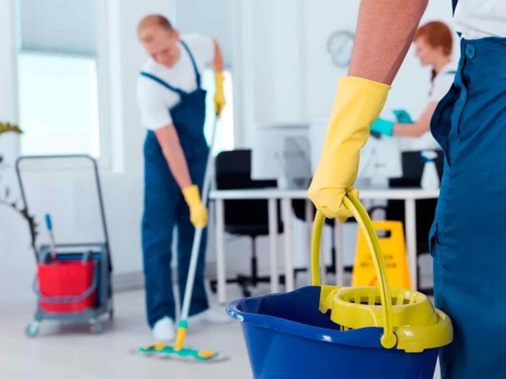 A person holding a mop and bucket in an office.