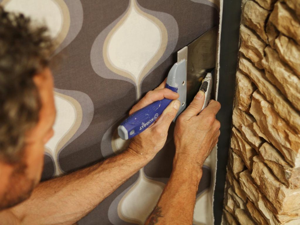 A man is using a spatula to paint the wall.