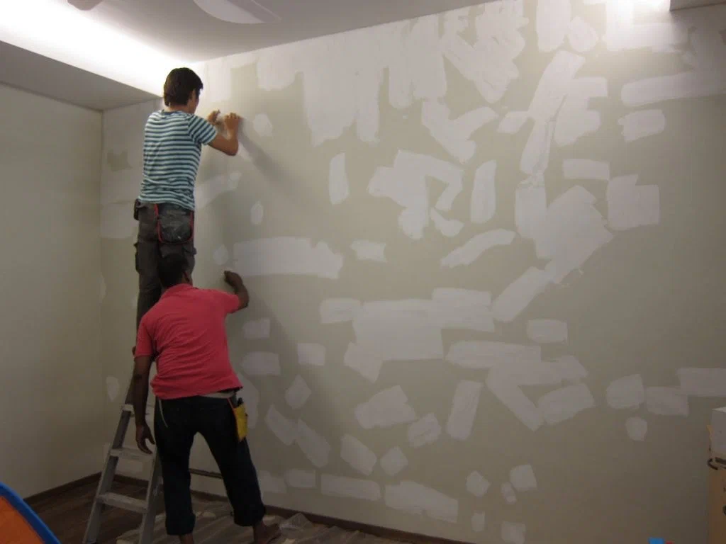 Two men are painting a wall with white paint.